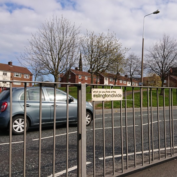 Laser-cut #IslingtonDivide sign fastened to a fence in the central reservation