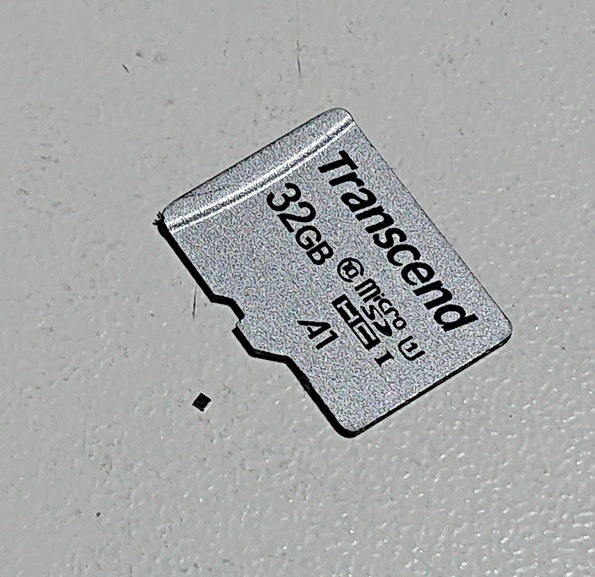 A micro-SD card on a white table with a tiny square black dot of a varicap next to it, barely visible