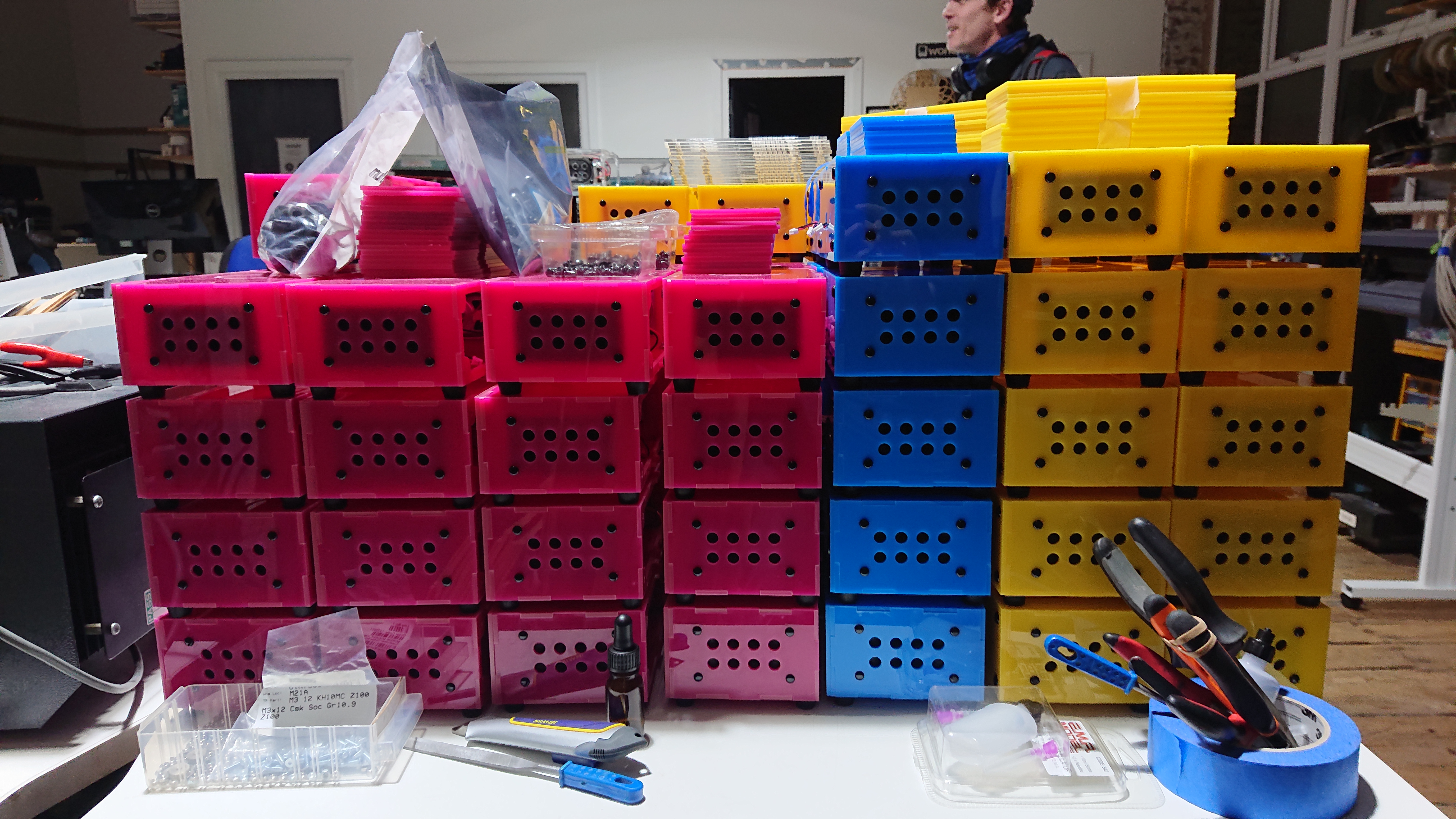 A desk in a makerspace with many brightly-coloured acrylic boxes stacked on top of each other, with a collection of tools and spare parts in front of them