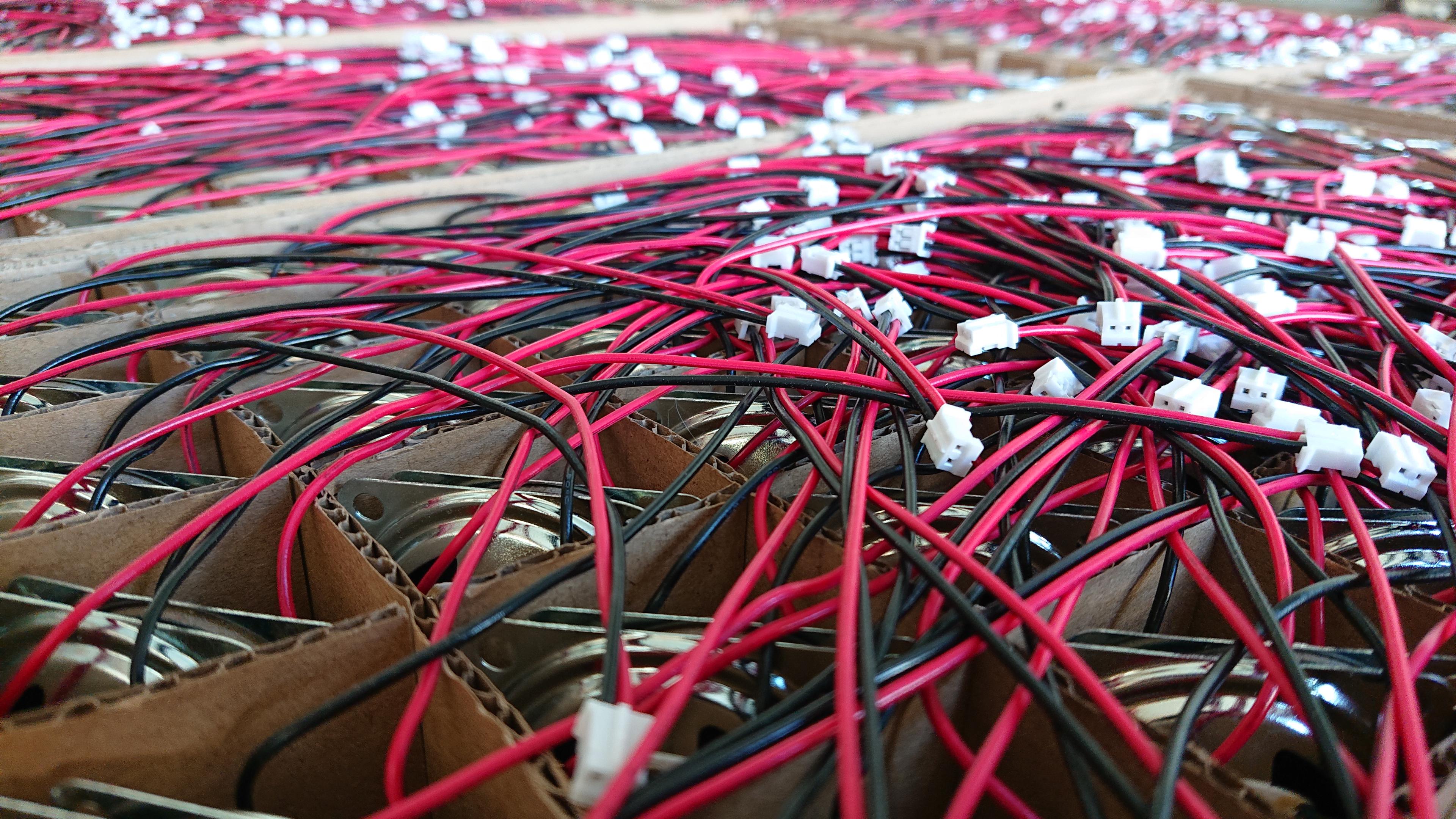Looking out across a sea of speakers, all slotted in pairs into a grid of gaps in the cardboard packaging.  Not that it's too easy to spot that they're speakers, the silver of the frame is just about visible in the ones nearest to us, and mostly it looks like a massed tangle of red and black wires dotted with white JST connectors