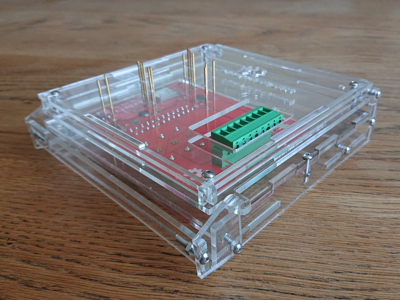 A transparent acrylic box whose lid is pierced by a collection of thin, gold pins which line up with key test points on the PCB which is held in place inside the box