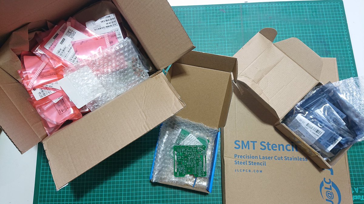 A collection of cardboard boxes containing lots of bags of electronic components, some PCBs and a stainless steel stencil