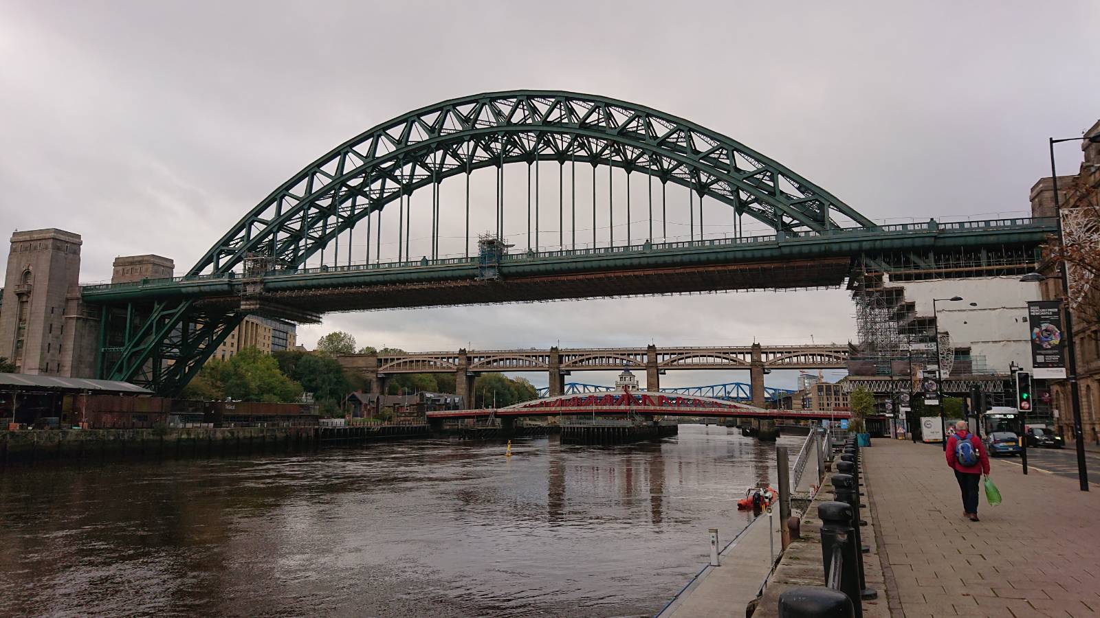 A photograph of the Tyne bridge taken from Newcastle. The bridge is a large steel arch, painted green, with stone pillars at either end and a road way running through it. Beyond this bridge three other bridges can also be seen spanning the Tyne.
